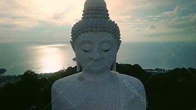 Kind face of Phuket big Buddha statue against sunset ocean