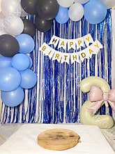 Birthday decoration featuring a backdrop of blue metallic streamers with a \"HAPPY BIRTHDAY\" banner