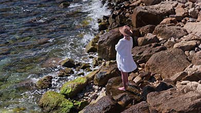 Middle aged woman standing on rocky Mediterranean shoreline looking at sea, travel freedom and peaceful lifestyle