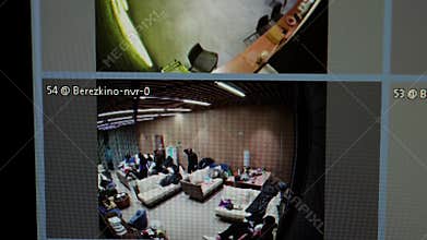 Security camera screens displaying refugee shelter interior, capturing displaced individuals gathering personal items