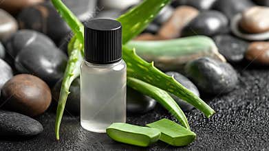 Clear glass bottle with black cap, surrounded by aloe vera and smooth rocks on a textured surface
