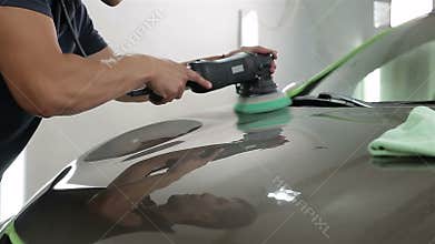 Close up shot of a man waxing hood of the car with special tool.
