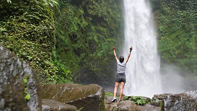 Young Traveler Girl Takes Raising Up Arms at Amazing Jungle Waterfall in Bali, Indonesia. 4K, Slowmotion Cinematic Travel