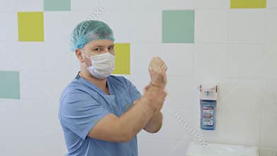 Surgeon in sterile clothing uses dispenser for disinfection hands before surgery