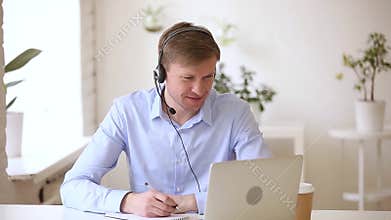Smiling businessman wearing headset studying online making notes