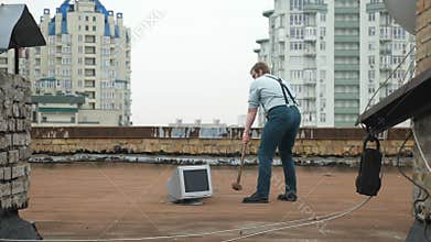 Young strong man smashes the monitor with a sledgehammer on the roof. Hammer, bat, violence, hatred, anarchy