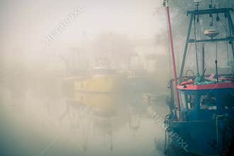 Fishing boats moored on a misty river.