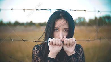 Girl brunette refugee behind barbed wire camp slow motion video. the concept of freedom is upset Woman lifestyle hands