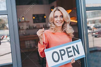 attractive middle aged small business owner holding sign open and smiling