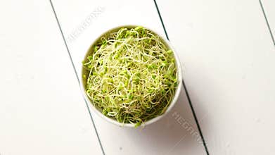 Bowl full of fresh radish sprouts placed on white wooden background