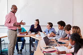 High School Teacher Talking To Pupils Using Digital Devices In Technology Class