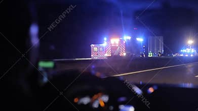 Driving by a car crash on highway at night. View from inside the car