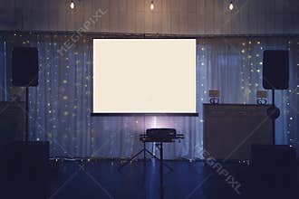Illuminated banquette hall stage with a big white screen and acoustic systems. Equipment for video and audio projection at a festi