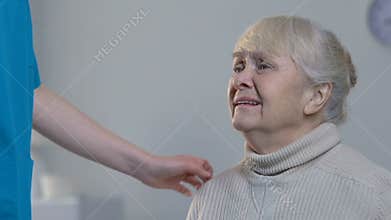 Medical worker comforting desperately crying elderly woman in nursing home