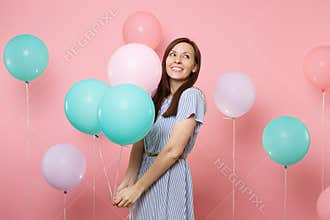 Portrait of pretty happy woman wearing blue striped dress dreaming looking up holding colorful air balloons on bright