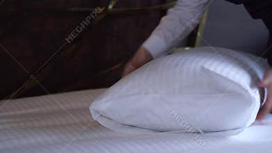 Maid straightens a pillow in a small, cozy hotel room.