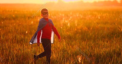 Little boy plays and dreams of a super hero at sunset