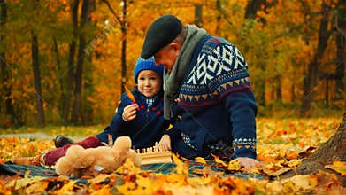 Little boy and his grandfather are sitting in the autumn park and playing with leaves