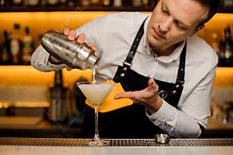Bartender pouring a fresh alcoholic drink into the cocktail glass