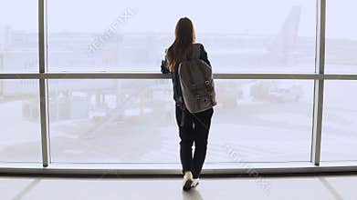 Young woman with backpack near terminal window. Caucasian female tourist using smartphone in airport lounge. Travel. 4K.