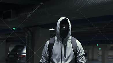 Man criminal in the balaclava and hood looking at the camera in underground parking,slow mo