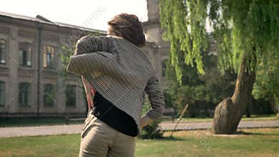 Young beautiful girl is dancing in park in daytime, in summer, movement concept, building on background, blured