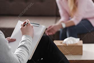 Close-up of therapist hand writing notes during a counseling session with a single woman sitting on a couch in the blurred
