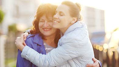 A mature mother and an adult daughter met on the street and embrace. Happy family, continuity of generations. Mothers