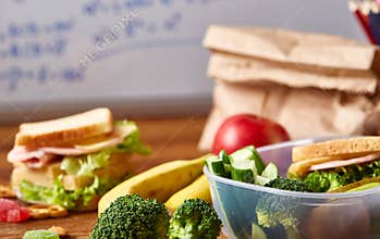 Back to School concept, school supplies, biscuits, packed lunch and lunchbox over white chalkboard, selective focus.