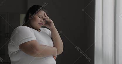 Frustrated overweight woman stands near window