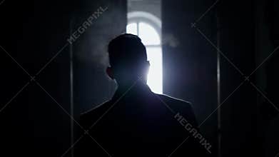 Silhouette of mature man walking along dark corridor towards empty bright room