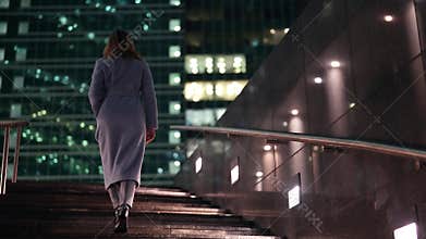 townswoman is dressed warm coat for fall season is walking in city in evening, going up over stair