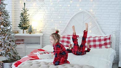 Two children in pajamas jump, hop and make funny face making faces on the bed in the bedroom with a Christmas tree.