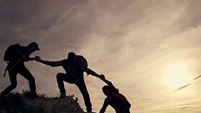 Teamwork of the business group. Male partners climb to the top. Silhouette of a helping hand at sunset. The concept of