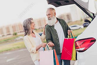 Photo of retired pensioner wife husband grey haired old couple shopper hold bags car outside outdoors in urban city