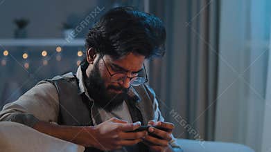 Close-up focused motivated inspired Arabian Indian man bearded guy in glasses playing mobile game online sports