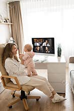 Young woman working at desk at home with computer holding crying tired infant baby holding business meeting at home