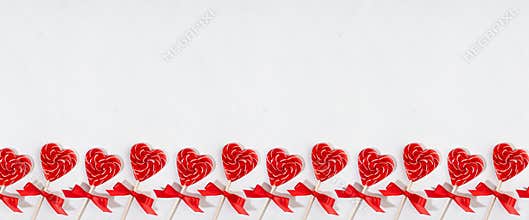 Fun valentines day background - sweet red lollipops hearts with bows on white wood board as decorative seamless border for banner.