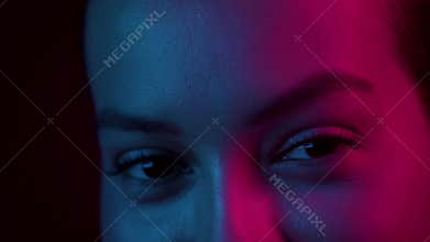 Female eyes blinking under neon blue pink light. Girl with beautiful face and makeup, close up. Nightlife concept