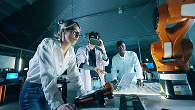 Three engineers at robotics development laboratory. Male engineer in VR headset operating robot