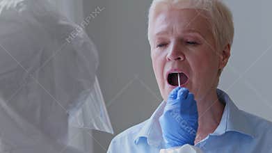 Old gray-haired woman sick elderly mature lady female patient opens mouth for pcr analysis doing covid-19 virus test