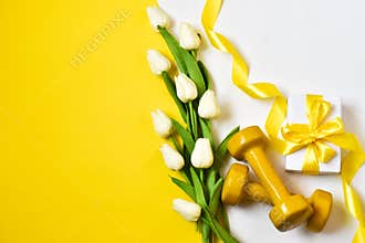Yellow dumbbells, gift present with boquet tulips on a yellow and white background.Healthy fitness. Postcard for Valentine`s Day,