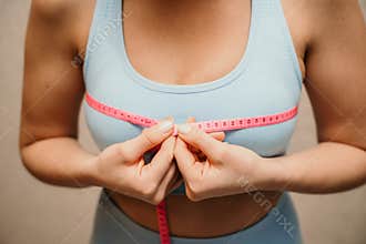 Cropped view of slim woman measuring breasts with tape measure at home, close up. Unrecognizable European woman checks