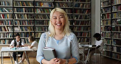 Smiling Asian student holding textbooks pose in campus library