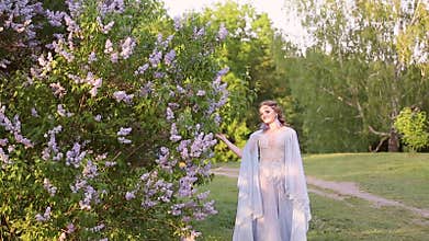 Beautiful woman in flying airy blue dress in blooming lilac garden.