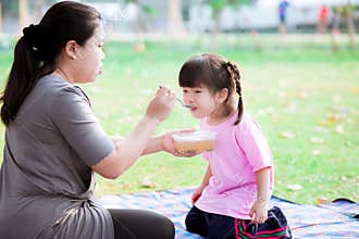 Picnic family concept. Mother was sitting and feeding soup to her daughter in the park.