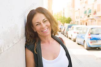 Beautiful middle age woman smiling cheerful leaning on a brick wall at the city street on a sunny day