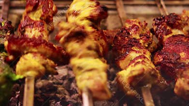 A kebab maker turns over kebabs of chicken, Seekh kebab roasting on skewers,