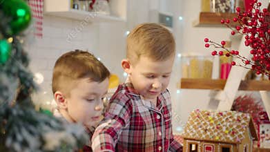 Cute boys decorating gingerbread house with topping and icing at the kitchen