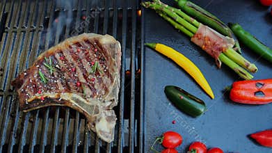 Beef T-Bone steak on the cooking grill with grilled vegetables. Slow motion